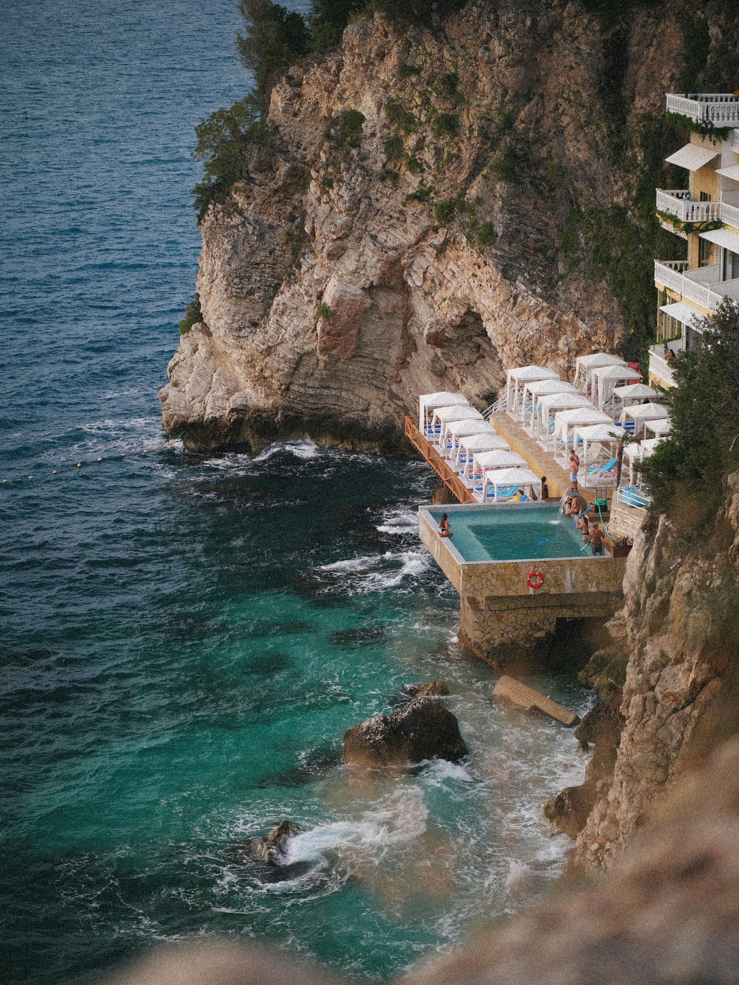 A cliff on the Albanian Riviera with a pool and cabanas above the turquoise sea